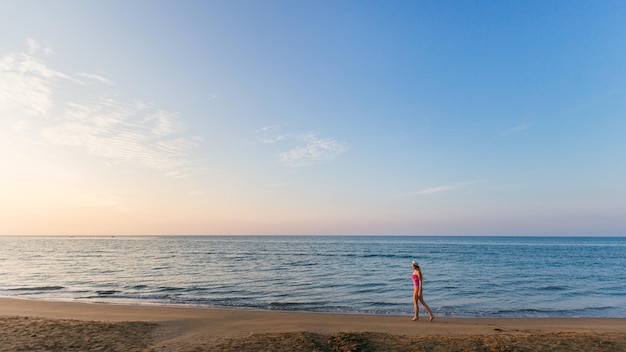 Fille marchant sur la plage sur le fond de la mer du soir