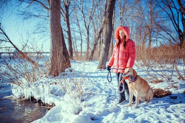 Fille marchant avec son labrador retriever jaune dans le paysage d'hiver