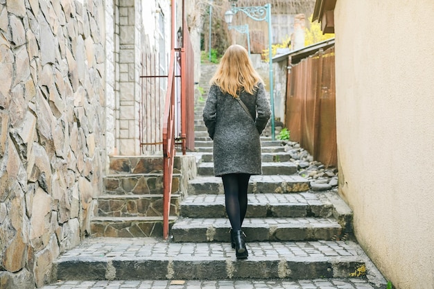 La fille marche dans la rue étroite avec une chaussée en pierre Femme élégante Lanterne médiévale Escaliers dans la ville