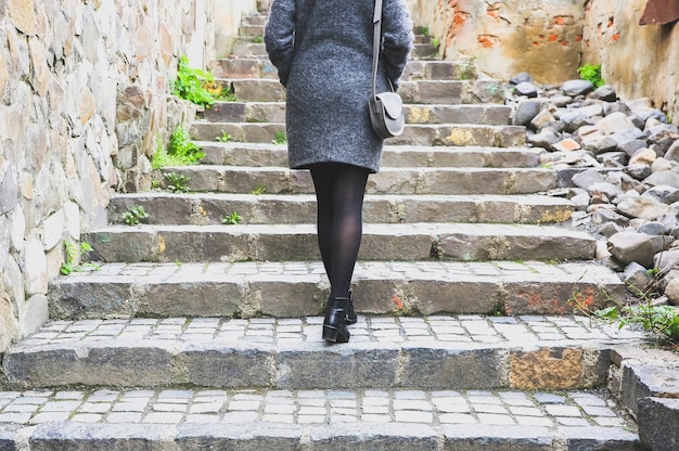 La fille marche dans la rue étroite avec le trottoir en pierre Femme élégante avec un sac en cuir. Escaliers dans la ville.