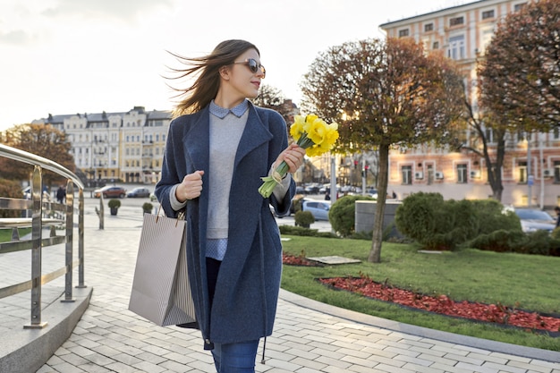 Fille marche dans la ville, jeune femme avec bouquet de fleurs et sac à provisions