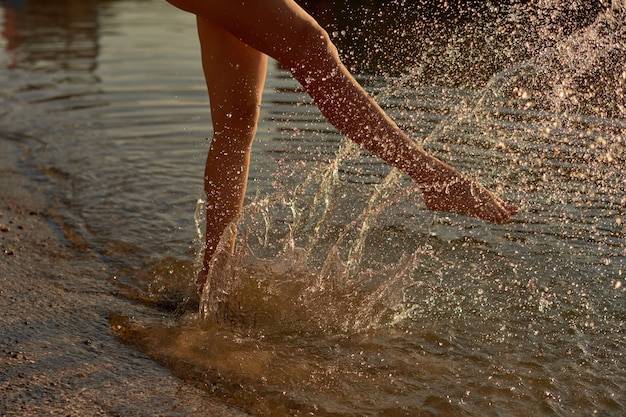 Une fille marche le long du bord de mer et crée des éclaboussures de vagues avec ses pieds nus