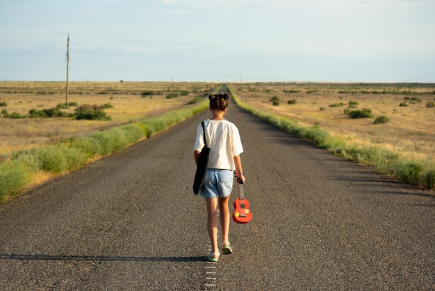 Une fille marche le long d'une route déserte dans la steppe Elle a un ukulélé et un sac à dos Route ouverte