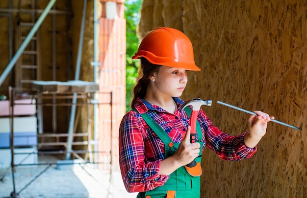 Fille martelant un concept de menuiserie et de menuiserie à ongles enfant adolescent à l'aide d'outils de construction et de réparation d'outils de marteau réparateur petite fille réparant dans l'atelier enfant joyeux dans le casque tenir le marteau