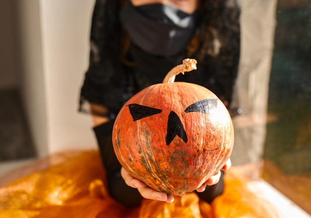 Fille en masque assis à la fenêtre à la maison en costume d'halloween avec citrouille Jack ou Laurent