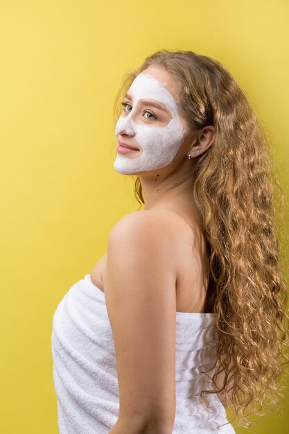 Fille avec un masque cosmétique sur son visage dans une serviette blanche