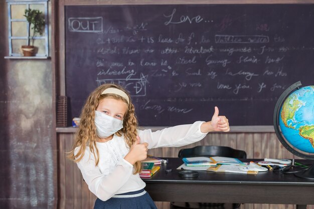 Fille avec masque facial de retour à l'école après la quarantaine covid et le verrouillage écolière écrivant en exerc...