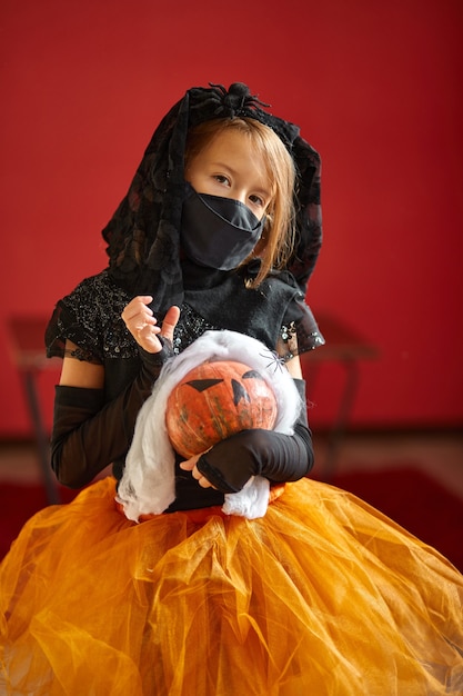 Fille en masque à la maison en costume d'halloween avec citrouille Jack ou Laurent