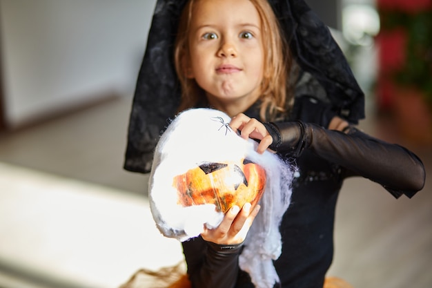 Fille en masque à la maison en costume d'halloween avec citrouille Jack ou Laurent