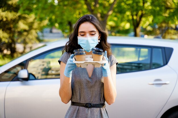 Fille en masque médical et gants tient le plateau de tasses à café jetables