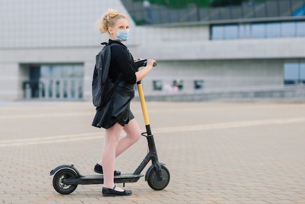 Fille avec un masque quittant sa maison pour aller à l'école sur un scooter