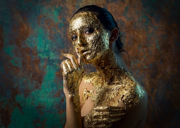 Fille avec un masque sur son visage fait de feuille d'or Portrait en studio sombre d'une brune sur un résumé