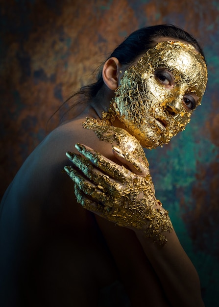 Fille avec un masque sur son visage fait de feuille d'or Portrait en studio sombre d'une brune sur un résumé