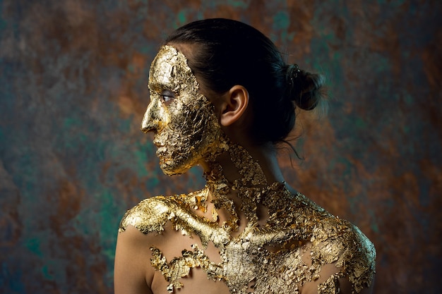 Fille avec un masque sur son visage fait de feuille d'or Portrait en studio sombre d'une brune sur un résumé