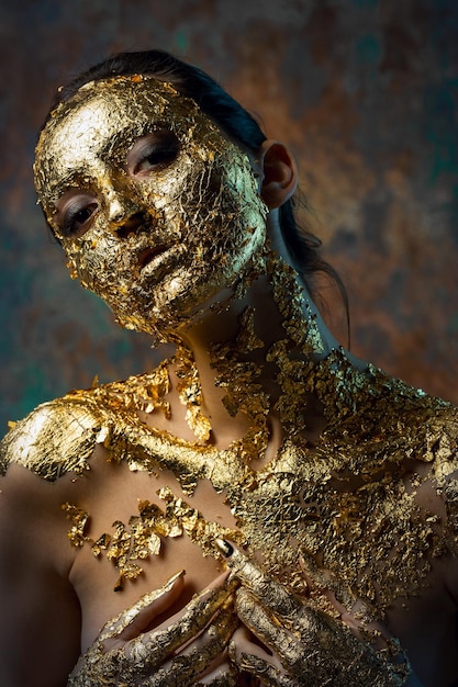 Fille avec un masque sur son visage en feuille d'or Portrait en studio sombre d'une brune sur un fond abstrait