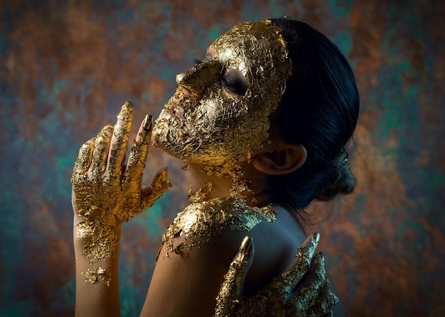 Fille avec un masque sur son visage en feuille d'or Portrait en studio sombre d'une brune sur un fond abstrait