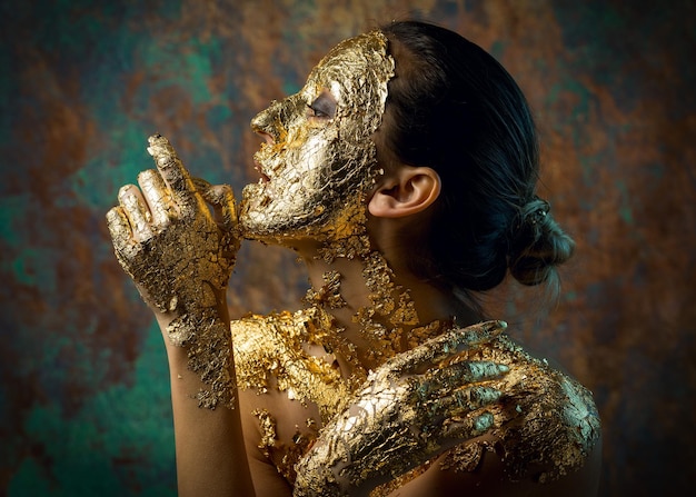 Fille avec un masque sur son visage en feuille d'or Portrait en studio sombre d'une brune sur un fond abstrait