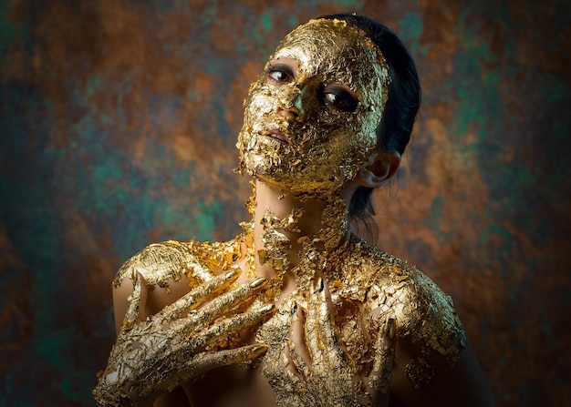 Fille avec un masque sur son visage en feuille d'or Portrait en studio sombre d'une brune sur un fond abstrait