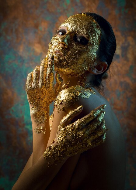 Fille avec un masque sur son visage en feuille d'or Portrait en studio sombre d'une brune sur un fond abstrait