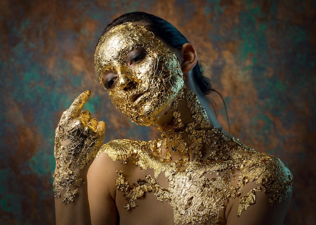 Fille avec un masque sur son visage en feuille d'or Portrait en studio sombre d'une brune sur un fond abstrait