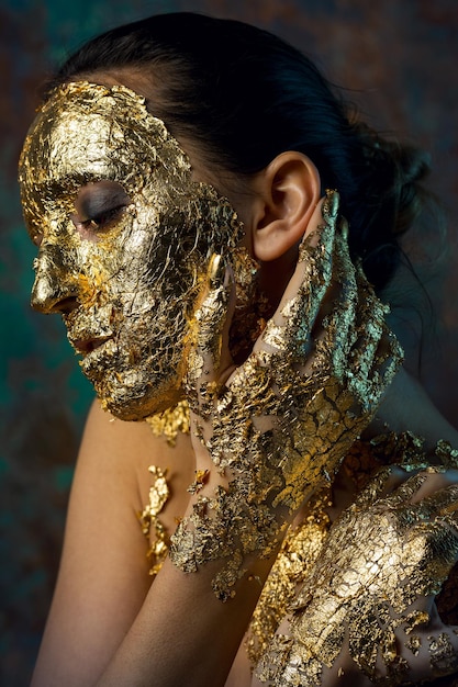 Fille avec un masque sur son visage en feuille d'or Portrait en studio sombre d'une brune sur un fond abstrait