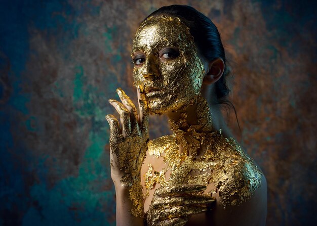 Fille avec un masque sur son visage en feuille d'or Portrait en studio sombre d'une brune sur un fond abstrait