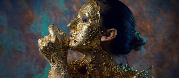 Fille avec un masque sur son visage en feuille d'or Portrait en studio sombre d'une brune sur un fond abstrait