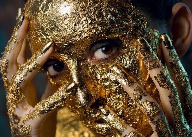 Fille avec un masque sur son visage en feuille d'or Portrait en studio sombre d'une brune