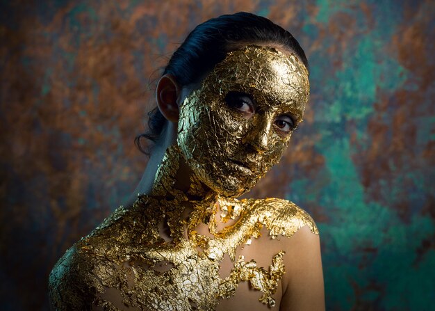 Fille avec un masque sur son visage en feuille d'or Portrait en studio sombre d'une brune