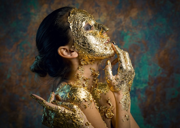 Fille avec un masque sur son visage en feuille d'or Portrait en studio sombre d'une brune