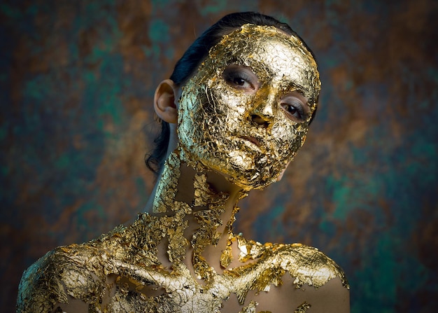 Fille avec un masque sur son visage en feuille d'or Portrait en studio sombre d'une brune