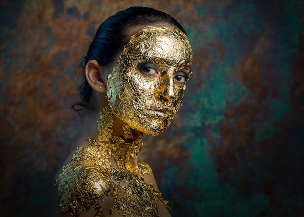 Fille avec un masque sur son visage en feuille d'or Portrait en studio sombre d'une brune