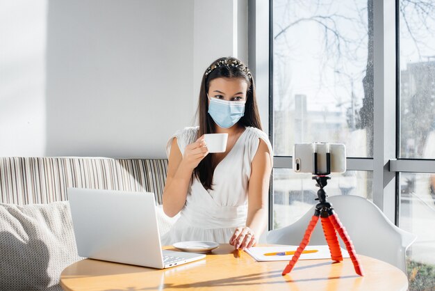 Une fille masquée est assise au bureau et tourne des blogs vidéo.