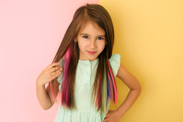 Fille avec des mèches de cheveux teints colorés isolés sur un fond de studio rose et jaune