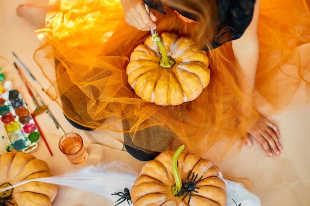 Fille méconnaissable décorant une citrouille orange, dessin visage Jack-O-Lantern pour Halloween