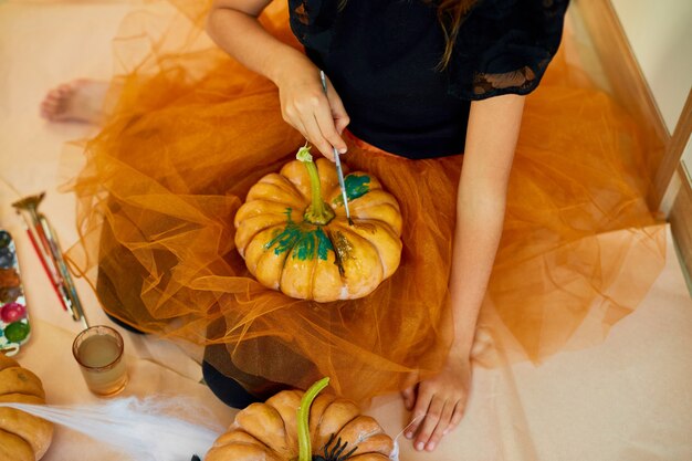 Fille méconnaissable décorant une citrouille orange, dessin visage Jack-O-Lantern pour Halloween