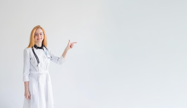 Une fille médecin aux cheveux rouges pointe son doigt sur le côté sur un fond blanc fond isolé est l'endroit pour l'inscription