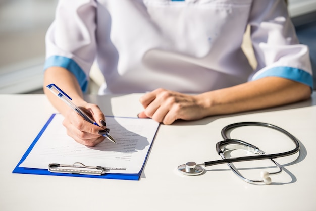 Fille médecin est assis à une table et écrit.