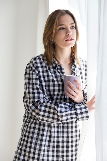 Fille mélancolique prenant un café en regardant par la fenêtre