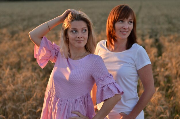 une fille et une mère dans un champ de blé sourient et parlent négligemment