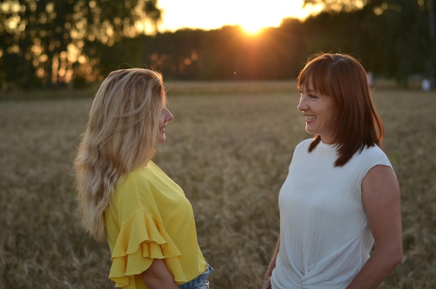 une fille et une mère dans un champ de blé sourient et parlent négligemment