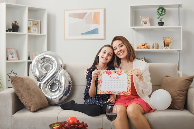 Fille et mère heureuses le jour de la femme heureuse tenant un calendrier assis sur un canapé dans le salon