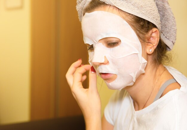 Fille met une feuille de masque de peau sur le visage Procédures de beauté à la maison