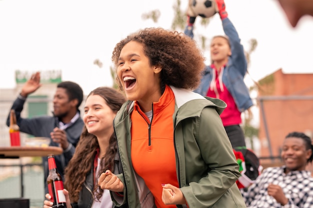 Fille métisse extatique et ses amis interculturels acclamant leur équipe de football après but