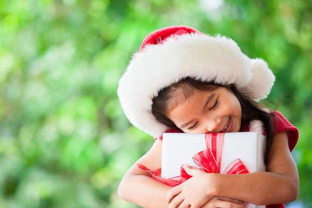 Fille mignonne enfant asiatique en bonnet rouge tenant un cadeau de Noël à la main