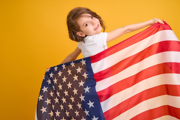 Fille mignonne d'enfant heureux avec le drapeau américain sur le jaune