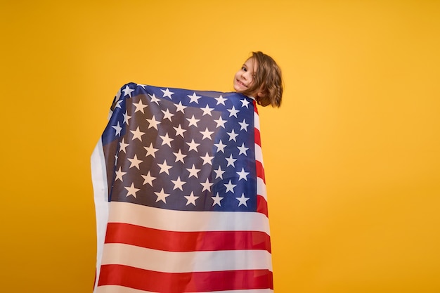 Fille mignonne d'enfant heureux avec le drapeau américain sur le jaune