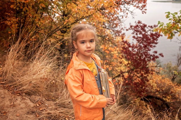 Fille mignonne intelligente tenant un livre avec des feuilles jaunes sèches