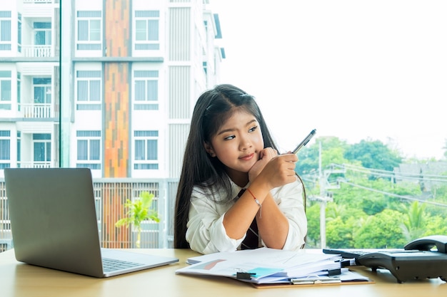 fille mignonne s&#39;asseoir chercher et tenant un stylo dans la chambre