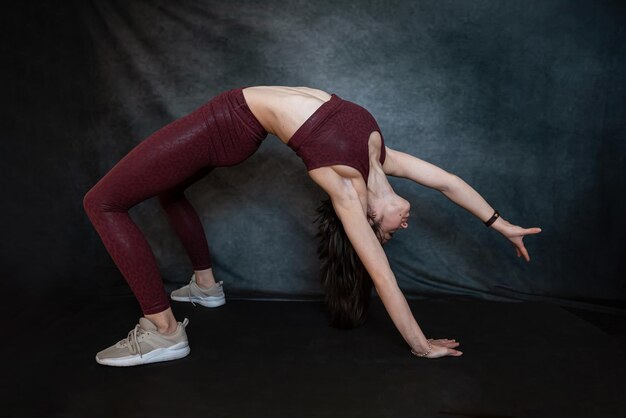 Une fille mince caucasienne en tenue de sport rouge fait des exercices d'étirement du matin sur fond de blackstudio